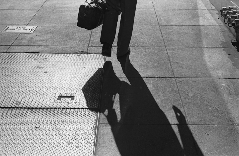 Strongly Backlit Black and White Photo of Concrete Sidewalk With Shadow of Walking Person.